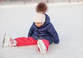 menina adorável sentada no gelo com patins após a queda foto