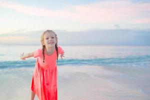 adorável menina na praia se divertindo muito à noite. criança feliz olhando fundo da câmera lindo céu e mar foto