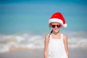 adorável menina com chapéu de Papai Noel em praia tropical foto