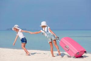 meninas de turistas com mala grande na praia branca tropical foto