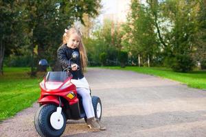 menina bonita do rock na jaqueta de couro sentada em sua motocicleta de brinquedo foto