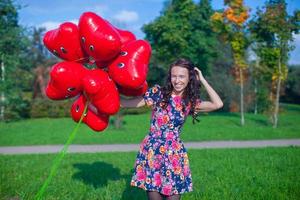 jovem mulher atraente feliz em lindo vestido com balões vermelhos andando lá fora foto