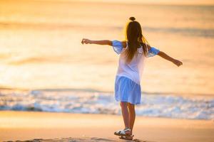 adorável menina feliz andando na praia branca ao pôr do sol. foto