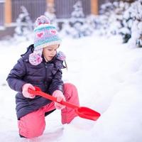 menina brinca com pá de neve em um dia de inverno foto