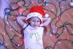 menina feliz encontra-se entre as luzes multicoloridas em um piso de madeira foto