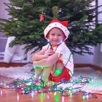 menina bonita com chapéu de papai noel sentado debaixo da árvore de natal entre guirlandas foto