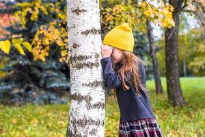 menina brincando de esconde-esconde na floresta de outono ao ar livre foto