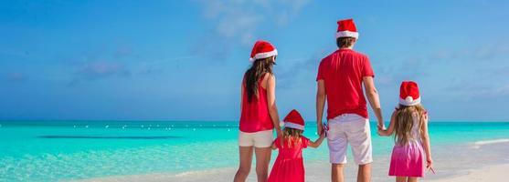 família de quatro pessoas feliz em chapéus de natal na praia branca foto