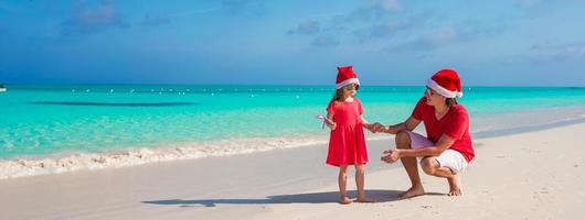 menina, pai feliz no chapéu de Papai Noel na praia exótica