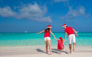 família feliz em chapéus de natal se divertindo na praia branca foto