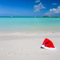 feliz natal escrito na areia branca da praia tropical com chapéu de natal foto