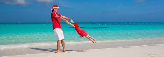 menina e pai feliz com chapéu de Papai Noel se divertem na praia tropical foto