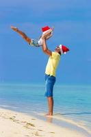 menina e pai feliz com chapéu de Papai Noel durante as férias na praia foto