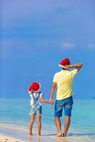 menina e pai feliz com chapéu de Papai Noel durante as férias na praia foto