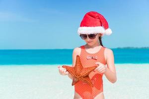menina feliz com chapéu de papai noel durante as férias na praia de natal divirta-se muito foto