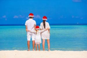 família feliz de três em chapéus de papai noel durante as férias tropicais