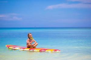 menina com pirulito divirta-se na prancha de surf no mar foto