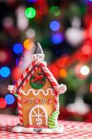 casa de fada de gengibre decorada por doces coloridos em um fundo de árvore de natal brilhante com guirlanda foto