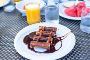 deliciosos waffles com chocolate, água e suco servidos no café da manhã no café ao ar livre foto