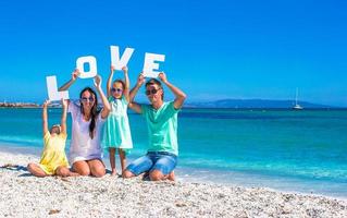 jovem linda família de quatro pessoas com a palavra amor na praia foto