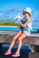 menina feliz com avião de brinquedo nas mãos na praia de areia branca foto