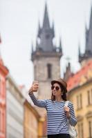 garota feliz tirando selfie fundo famoso castelo na cidade europeia. turista caucasiano caminhando pelas ruas desertas da europa. foto