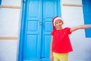 adorável garotinha com chapéu de Papai Noel tirando selfie na porta azul de fundo de rua estreita foto