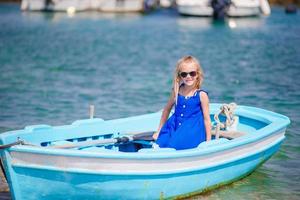 menina no barco azul na baía do mar na grécia. criança gosta de nadar no pequeno barco. foto