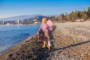 menina com asas de borboleta correndo ao longo da praia em um dia ensolarado de inverno foto