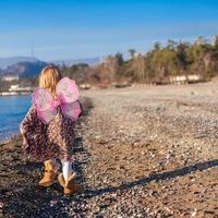 menina com asas de borboleta correndo ao longo da praia em um dia ensolarado de inverno foto