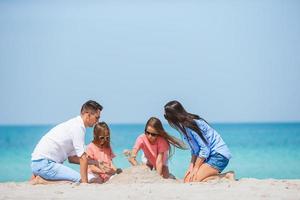 família de pais e filhos brincando com areia na praia tropical foto