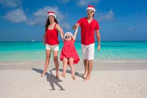 família feliz em chapéus de natal se divertindo na praia branca foto