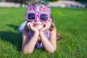 menina adorável em óculos de feliz aniversário sorrindo ao ar livre foto