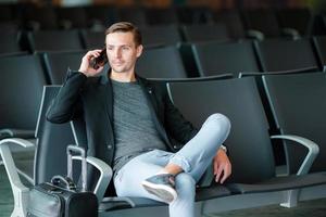 homem de negócios urbano falando no telefone inteligente viajando dentro do aeroporto. casual jovem empresário vestindo paletó. belo modelo masculino. jovem com celular no aeroporto enquanto aguarda o embarque. foto