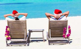 jovem casal de chapéu de papai noel relaxando na praia durante as férias de natal