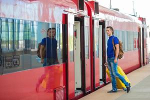 jovem homem caucasiano com bagagem na estação viajando de trem foto