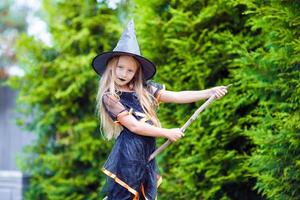 adorável menina vestindo fantasia de bruxa com vassoura no halloween ao ar livre foto