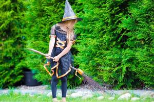 adorável menina vestindo fantasia de bruxa com vassoura no halloween ao ar livre foto