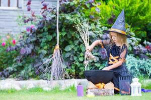 adorável menina vestindo fantasia de bruxa com vassoura no halloween ao ar livre foto