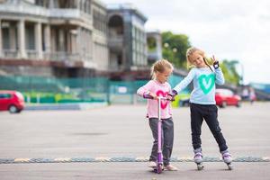 duas garotinhas patinando e andando de scooter no parque ao ar livre foto