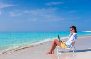 jovem trabalhando no laptop na praia tropical foto