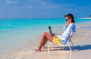 jovem empresário usando laptop na praia tropical foto