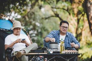 retrato de homem relaxado asiático usando smartphone e esperando seu amigo cozinhar foto