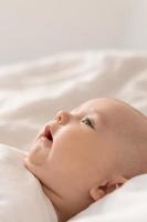 retrato de um bebê fofo em uma roupa branca em uma cama em casa com lençóis brancos. bebê recém-nascido em casa, maternidade feliz. foto de alta qualidade