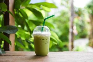 Smoothie de chá verde de bebidas geladas - chá verde matcha com leite em um copo de plástico na mesa de madeira e fundo verde natural foto