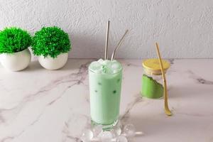 matcha dalgon chá verde em um copo alto com canudo de metal e pedaços redondos de gelo. pó de chá verde em uma jarra de vidro. uma alternativa ao café frio. foto