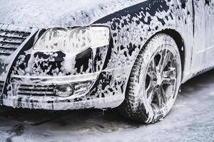o carro no lava-rápido é coberto com espuma, lave sob pressão com jato de água foto