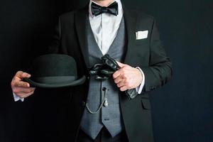 retrato de homem de terno escuro segurando luvas de couro e chapéu-coco. conceito de cavalheiro inglês clássico. estilo retrô e moda vintage. foto