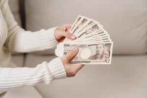 mão de uma mulher segurando a pilha de notas de iene japonês. dinheiro de mil ienes. dinheiro do japão, impostos, economia de recessão, inflação, investimento, finanças e conceitos de pagamento de compras foto
