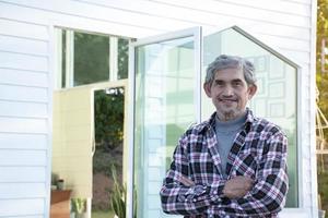 retrato idoso homem asiático sênior senta-se perto da janela de vidro pela manhã para trabalhar em casa e verificando seus negócios em seu laptop na mesa com foco sério, suave e seletivo. foto